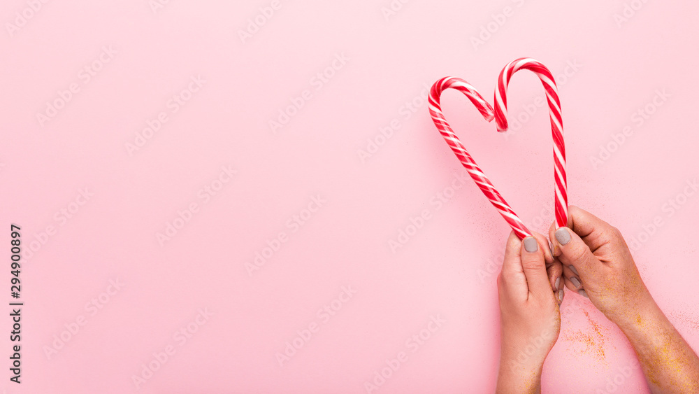 Fototapeta premium Candy cane in shape of heart in woman hands on pink