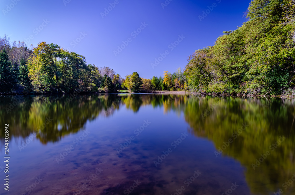 Fall trees reflected in a quiet pond under a clear blue sky.