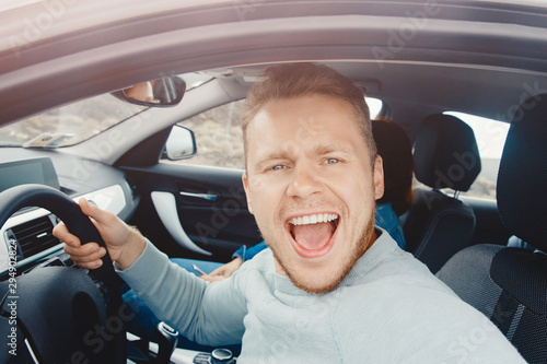 Male driver smiles and takes selfie photo. Car travel rental concept