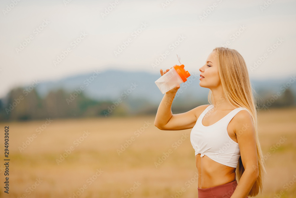 Beautiful blonde drinks water after workout in park from sports bottle Beautiful blonde drinks water after workout in park from sports bottle