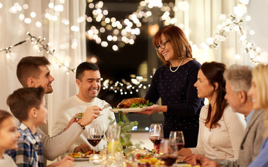 celebration, holidays and people concept - happy senior woman offering roast chicken to family having dinner party at home