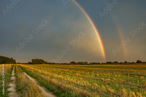 Two rainbows in the cloudy sky, horizon and dirt road in the field
