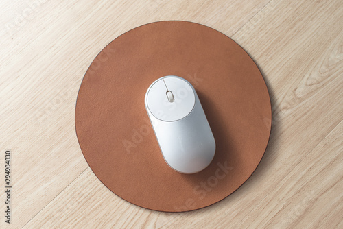 White and silver wireless mouse on a light brown round leather mouse pad on a wooden surface. photo