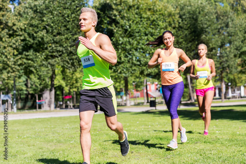 fitness, sport, race and healthy lifestyle concept - group of happy people or sportsmen running marathon with badge numbers at summer park