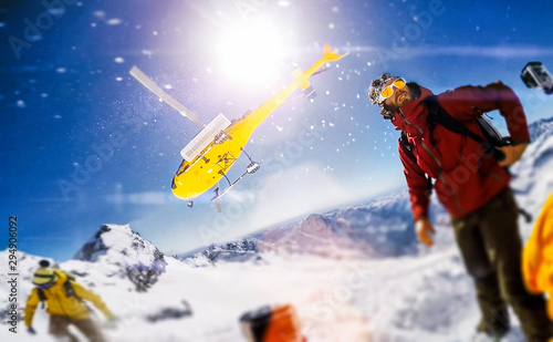 Actionsportlers were dropped by a helicopter at the top of the mountains while one person is taking a smile selfie with a wide angle camera.  The sun is shining brightly in the blue sky. There is a mo