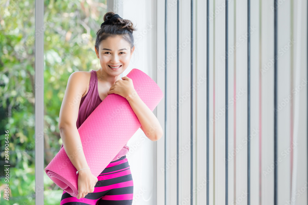 Portrait of a asian women workout practicing yoga in pink dress Hugs the Yoga mat roll pink and practice meditation wellness lifestyle and health fitness concept in a gym. Portrait of a asian women workout practicing yoga in pink dress Hugs the Yoga mat roll pink and practice meditation wellness lifestyle and health fitness concept in a gym.
