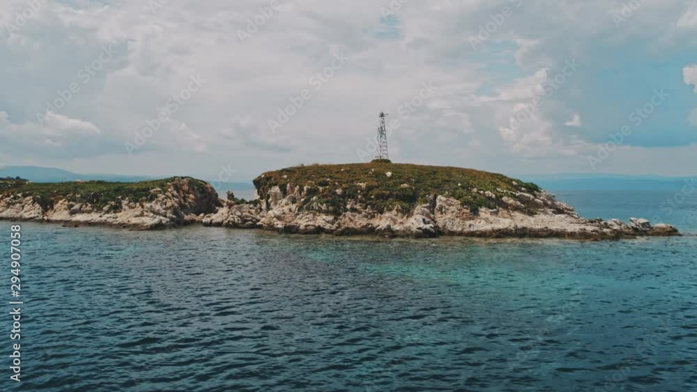 Drone aerial semi-circular shot of island with tower and sea around under sunny cloudy sky. Top view of island and water around under cloudy sky and mountains on background Drone aerial semi-circular shot of island with tower and sea around under sunny cloudy sky. Top view of island and water around under cloudy sky and mountains on background