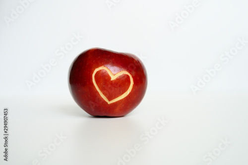Beautiful bright juicy ripe red apple with a heart shaped cut-out, located on a white background.