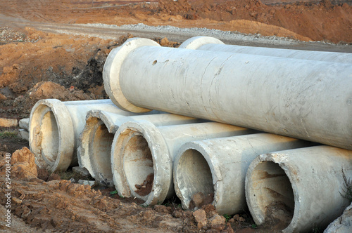 A wide-angle view of two rows of cement or concrete soil pipes lying on the ground, used to create sewage systems and aqueducts