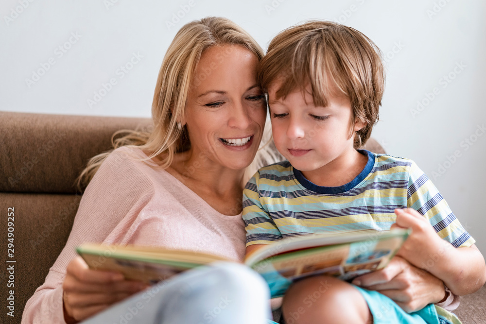 Mother and son reading a book together on couch at home Mother and son reading a book together on couch at home