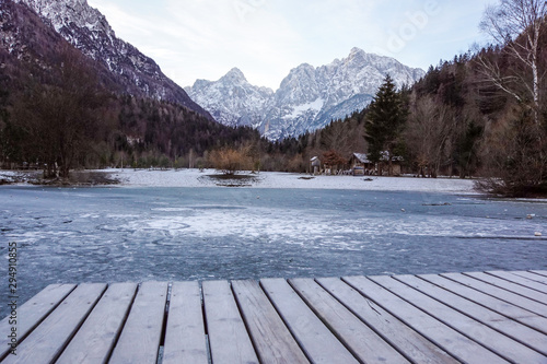 lake with green forest and snowy mountains in the background and skyfall effect. Italian lake during winter with mountains reflections