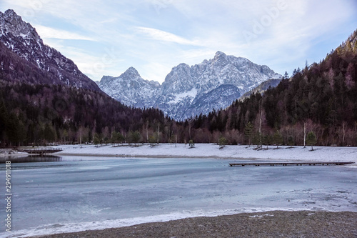 Beautiful view at sunset of the peaceful lake Fucine Tarvisio, Italy with green forest and snowy mountains in the background .