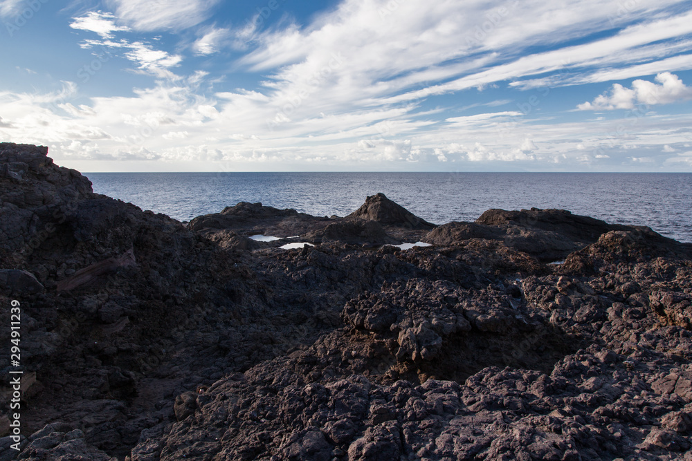 piedras volcánicas con mar adentrándose y nubes blancas