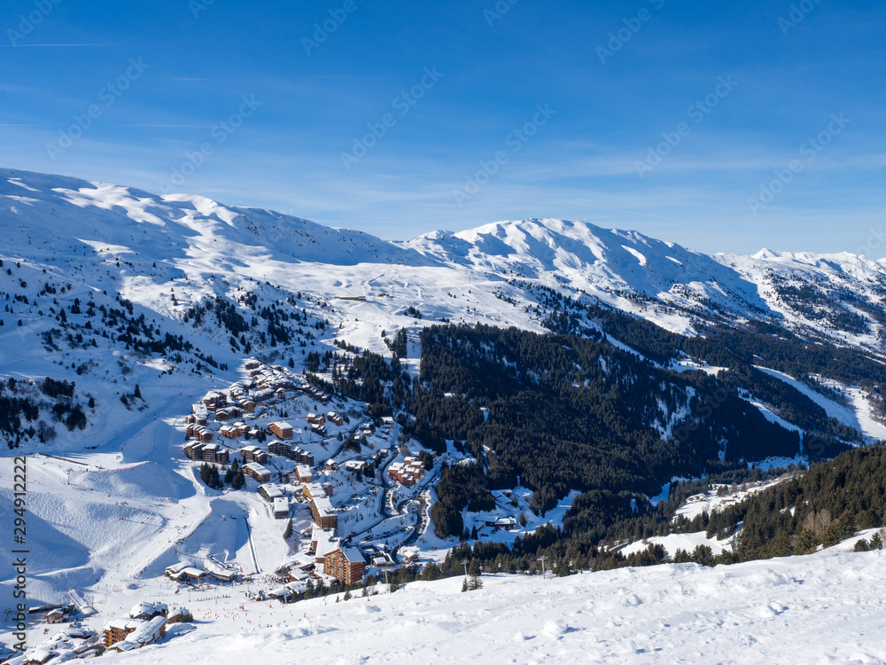 Meribel, France - February, 2018: Wooden Houses in Meribel ski resort. Skiers and snow slopes, beautiful sunny day.