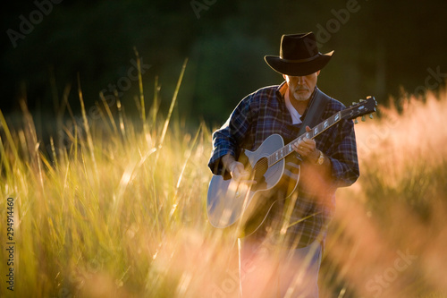 Mature man wearing a hat and strumming an acoustic guitar outdoors.