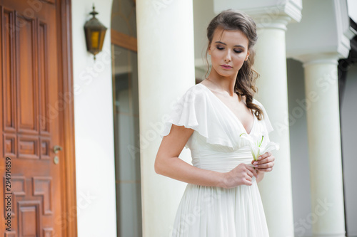 Young elegant woman with wedding bouquet in a light long white dress  before ceremony
