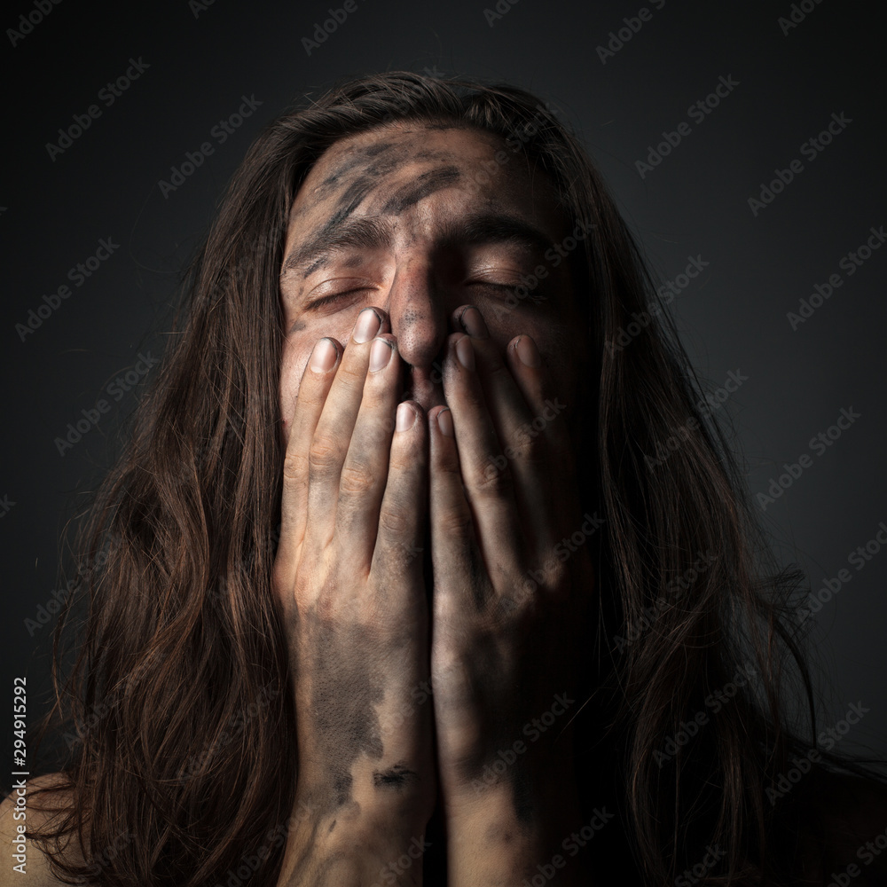 Fototapeta premium Portrait of a unhappy young man in soot. Hands on face