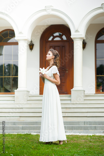 Beautiful young woman walking in long white dress. Tender bride with wedding bouquet.