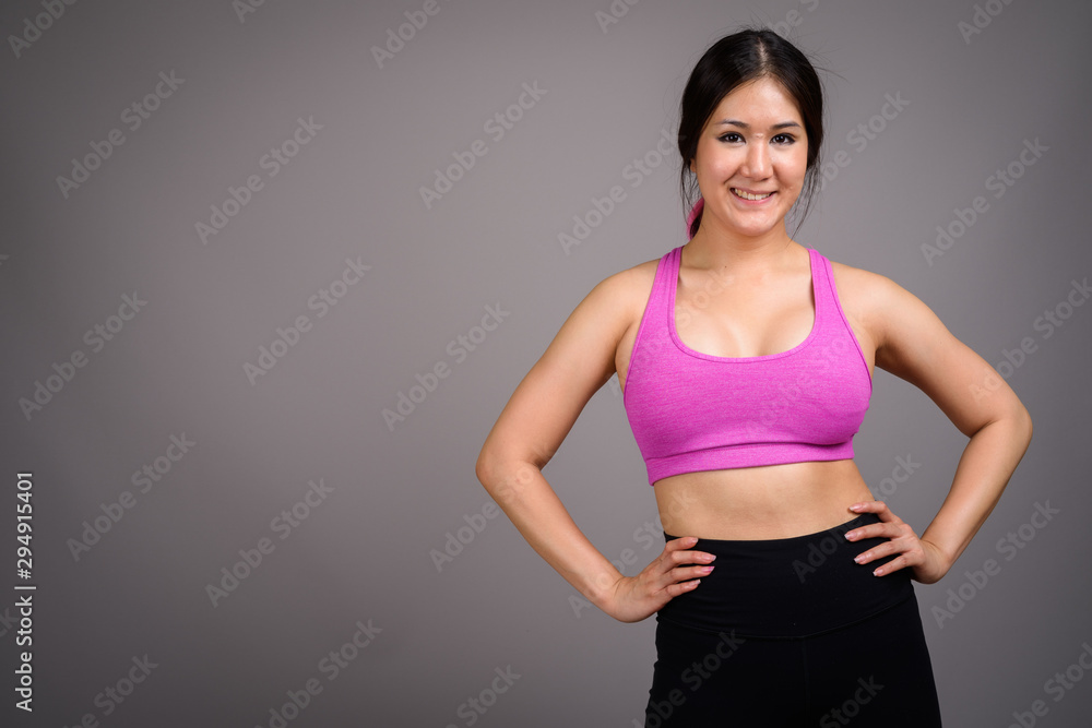 Young beautiful Asian woman ready for gym against gray backgroun Young beautiful Asian woman ready for gym against gray backgroun