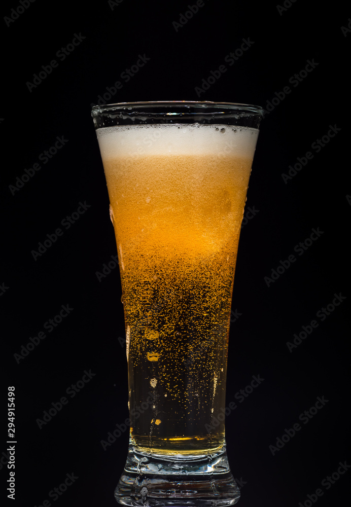 Glass of beer with foam on a black background in the dark