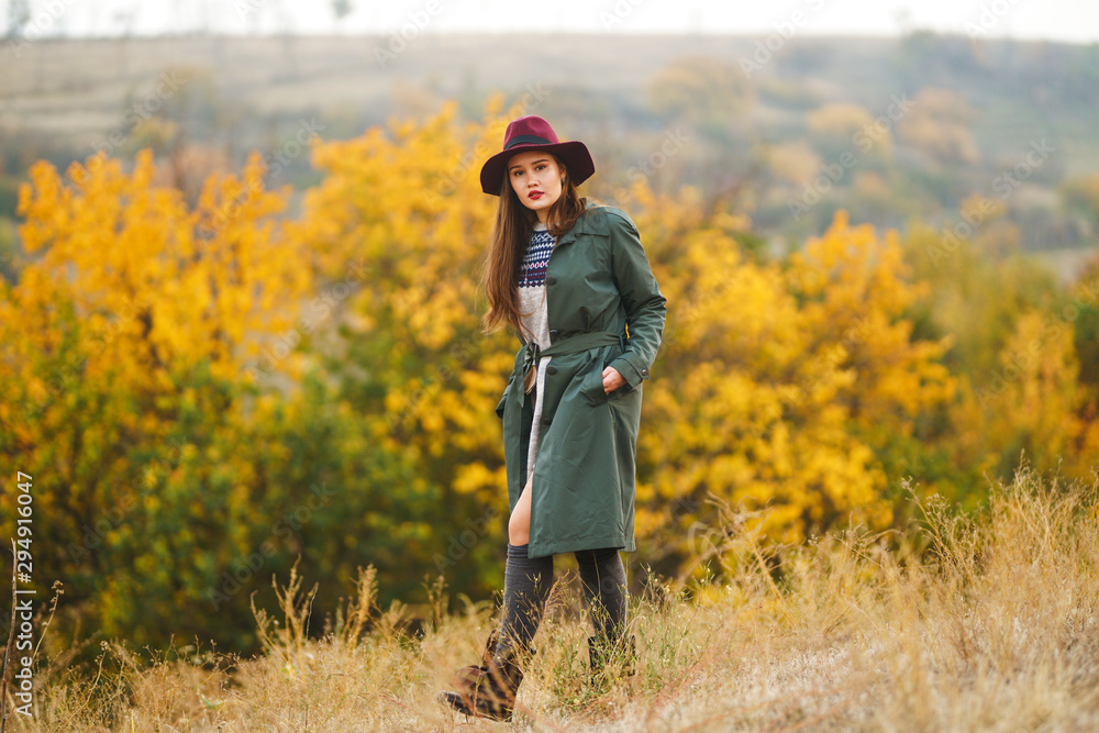 Beautiful young stylish girl in a coat walks in the autumn in the park. The girl is dressed in a green coat and a red hat. Beautiful evening. Autumn fashion. Lifestyle. High fashion portrait. Beautiful young stylish girl in a coat walks in the autumn in the park. The girl is dressed in a green coat and a red hat. Beautiful evening. Autumn fashion. Lifestyle. High fashion portrait.