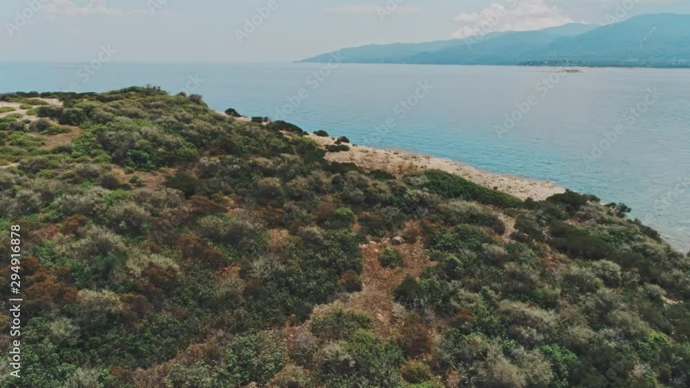 Drone aerial pan shot right to left of green rocky island and blue clear water under cloudy sky. Pan shot of island and ocean with mountains on background Drone aerial pan shot right to left of green rocky island and blue clear water under cloudy sky. Pan shot of island and ocean with mountains on background