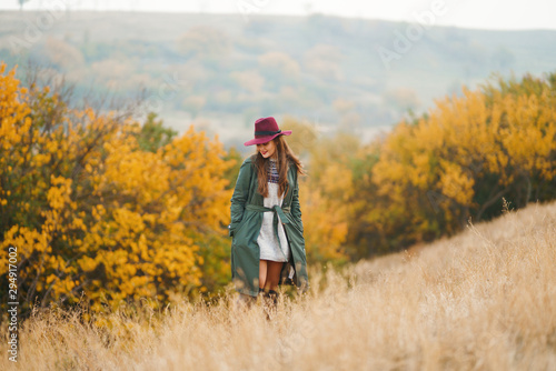 Beautiful young stylish girl in a coat walks in the autumn in the park. The girl is dressed in a green coat and a red hat. Beautiful evening. Autumn fashion. Lifestyle. High fashion portrait.  © maxbelchenko