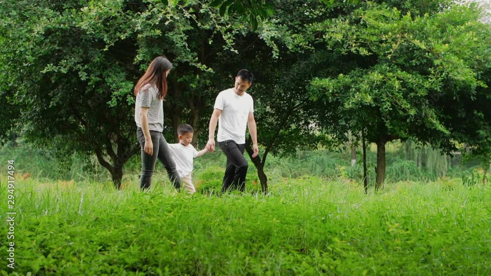 Slow motion side view of Chinese family walking together in the park parents holding son's hand jogging and talking family time outdoor Slow motion side view of Chinese family walking together in the park parents holding son's hand jogging and talking family time outdoor