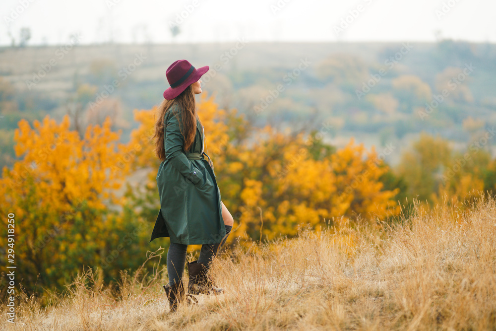 Beautiful young stylish girl in a coat walks in the autumn in the park. The girl is dressed in a green coat and a red hat. Beautiful evening. Autumn fashion. Lifestyle. High fashion portrait. Beautiful young stylish girl in a coat walks in the autumn in the park. The girl is dressed in a green coat and a red hat. Beautiful evening. Autumn fashion. Lifestyle. High fashion portrait.