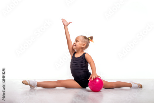 Studio shot of   attractive little  gymnast girl  with a pink ball doing twine on a white background.