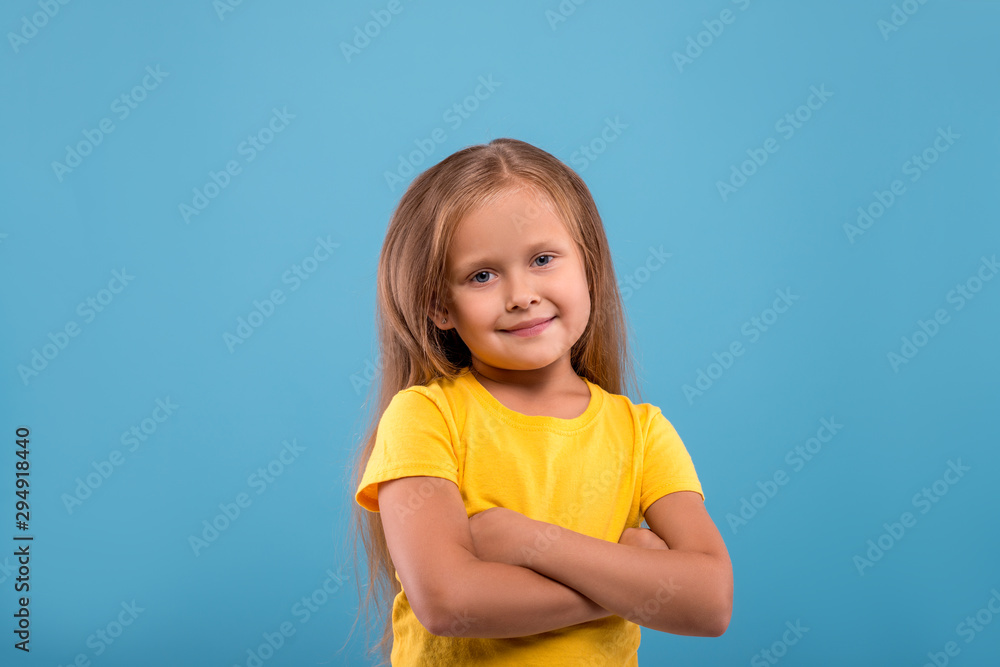 a smiling little girl with long blonde hair against blue background with copy space in studio. a smiling little girl with long blonde hair against blue background with copy space in studio.