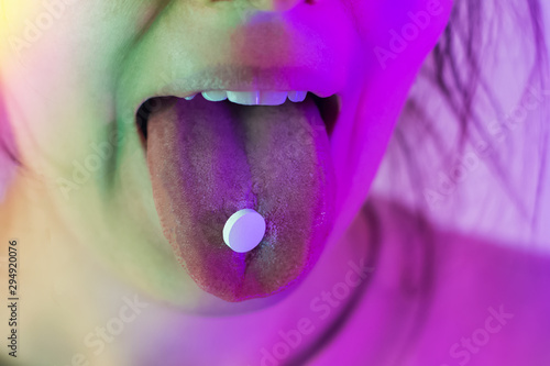 Fotografie Female tongue with a pill on it close-up in neon light.