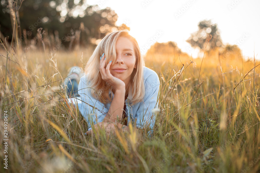 Fototapeta premium Beautiful young woman lying on the grass under light of sunset