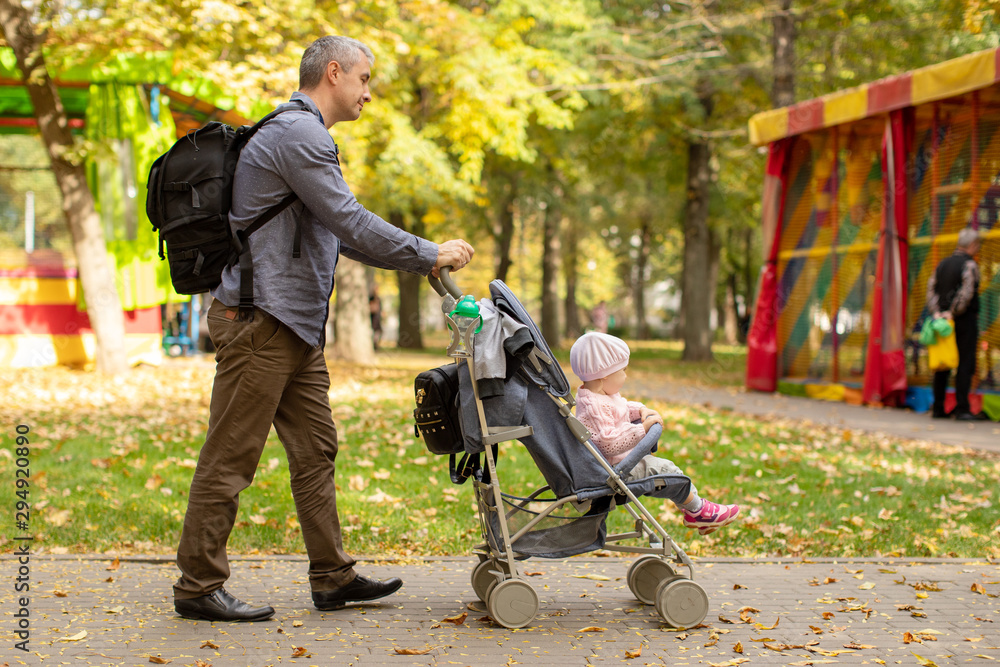 Obraz premium Man with baby stroller walks in the autumn park at sunset