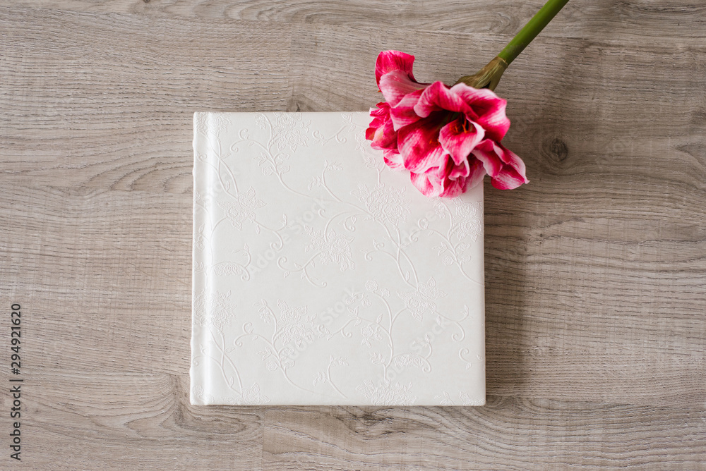 Wedding photo book in lace leather cover on beige background and bright pink flower next to it