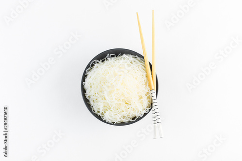 Cellophane rice noodles in a black bowl with chopsticks on white background, isolate, top view