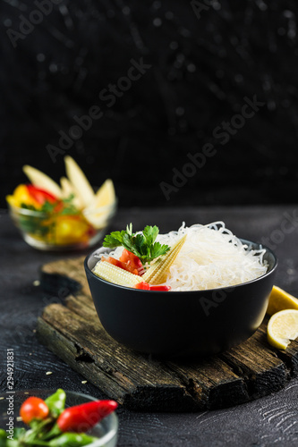 Cellophane rice noodles with vegetables in a black bowl with chopsticks on dark background, side view closeup. photo