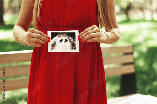 Happy young adult pregnant girl holds in her hands a snapshot of an ultrasound scan of a child. Twins. Two fetal eggs. First trimester.