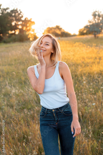 Young woman walking on the field at sunset and smiling