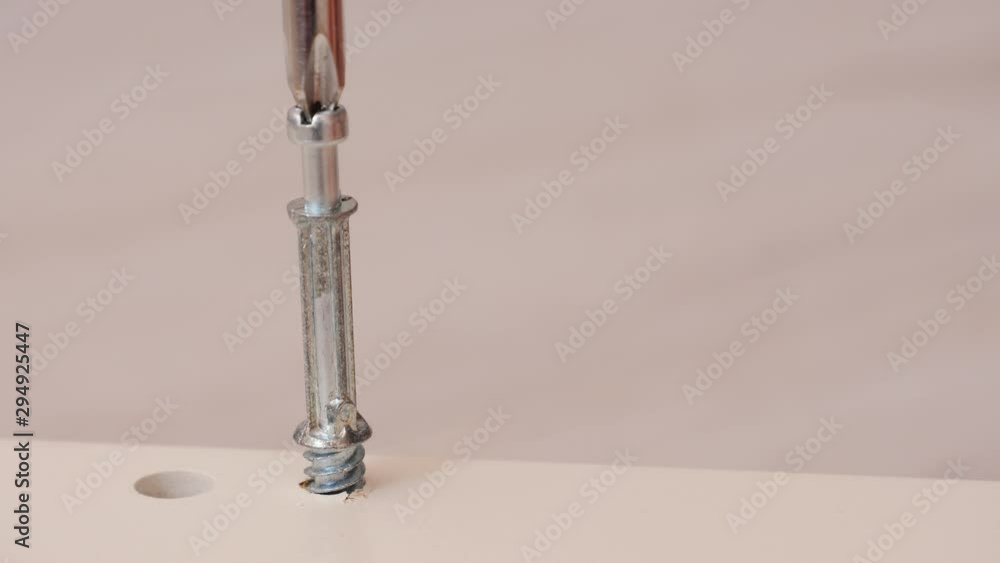 Assembling furniture at home. Mounting screw is screwed into hole board. Closeup of tool in hand. Do it yourself furniture assembly Assembling furniture at home. Mounting screw is screwed into hole board. Closeup of tool in hand. Do it yourself furniture assembly