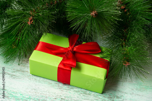 A wrapped green gift with a red ribbon lies under a Christmas tree on a wooden floor
