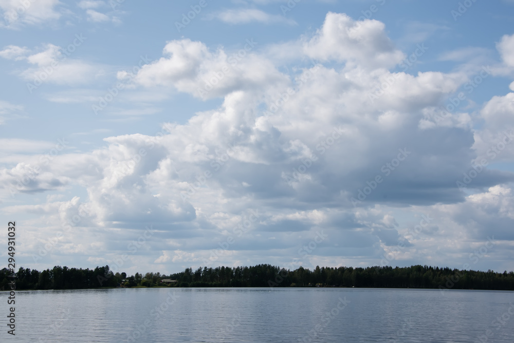 Summer view of the lake Hallanlahti with clouds on blue sky .