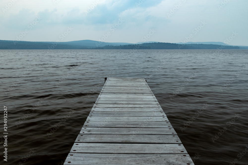 An Old Wooden Dock Jutting Out Into A Dark And Gloomy Lake With Cold Water