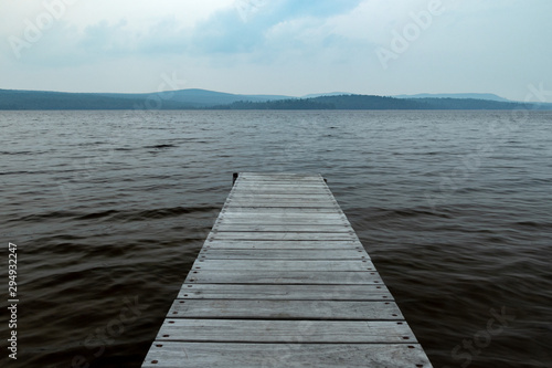 An Old Wooden Dock Jutting Out Into A Dark And Gloomy Lake With Cold Water