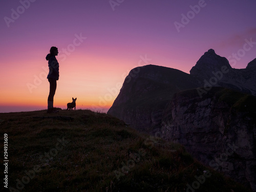 SILHOUETTE: Female hiker and her puppy reach the mountaintop on a summer evening