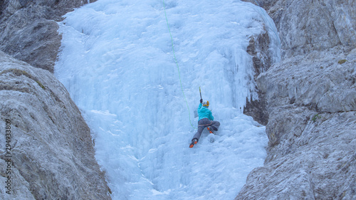 Athletic woman with crampons and ice axes scales the gorgeous frozen waterfall.