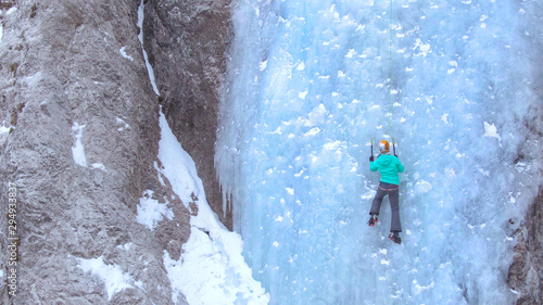 AERIAL  Unrecognizable woman climbs up a beautiful frozen waterfall in the Alps.