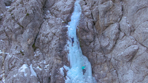 DRONE Flying towards a rocky wall as two ice climbers scale the frozen waterfall