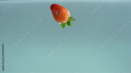 Fruits with strawberries are poured into clear and clean water.