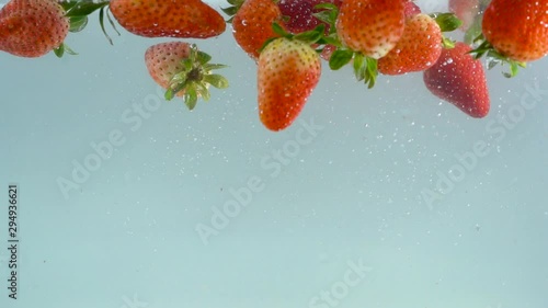 Fruits with strawberries are poured into clear and clean water.